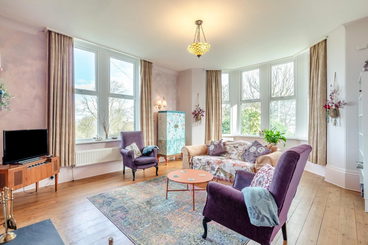 Ein Wohnzimmer mit Fernseher, zwei Sesseln, einer Couch, einem Couchtisch und einer Deckenleuchte.