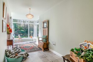 Ein geräumiger Raum mit großem Fenster, einer Holzbank, einem grünen Sessel und einem Korbkörbchen mit Pflanzen.