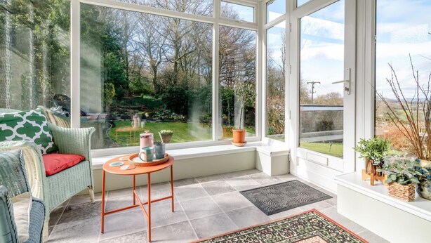 A conservatory with a view of a garden, a wicker sofa, a small table with items, and a potted plant. - 2 Bed in Shepley (oc-c36884) (Shepley)