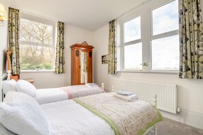 Ein Schlafzimmer mit zwei Betten, einem Holzschrank, einer Heizung und großen Fenstern mit floralen Vorhängen.