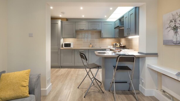 A compact kitchen with grey cabinets, a microwave, and a small island with seating. - 1 Bed in Hexham (oc-g37537) (Hexham)