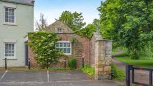 A brick building with a stone pillar, a gated entrance, and a paved driveway. - 1 Bed in Hexham (oc-g37537) (Hexham)