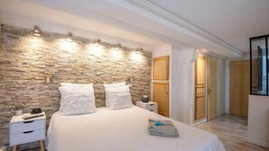 Ein Schlafzimmer mit Steinwand, einem Bett mit weißer Bettwäsche, einem Nachttisch und einer Holztür.