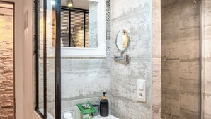 Ein Badezimmer mit Duschkabine aus Glas, einem weißen Waschbecken mit Pflegeprodukten und einem Spiegel an der Wand.