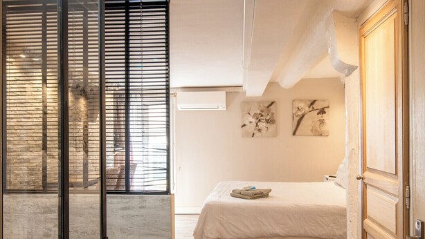 Ein Schlafzimmer mit einem Bett, einem Fenster mit Jalousien und zwei Wandbildern.