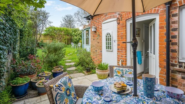 A patio with a table set for a meal, surrounded by potted plants and a brick wall.
