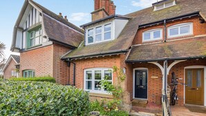 A two-story brick house with a front door, windows, and a small garden area.