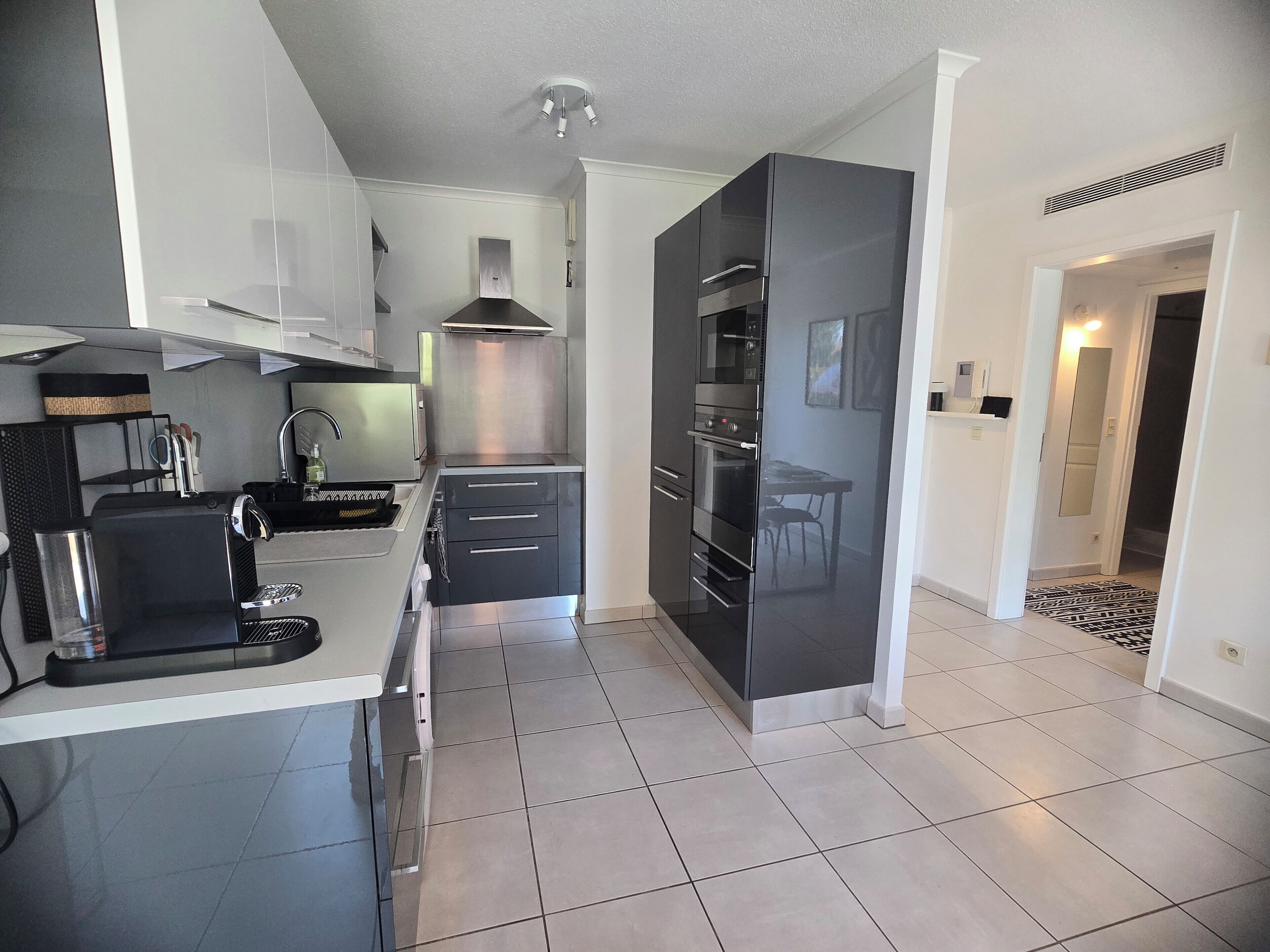 A modern kitchen with a built-in oven, a coffee machine, and a dining area with a table and chairs.