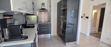 A modern kitchen with a built-in oven, a coffee machine, and a dining area with a table and chairs.