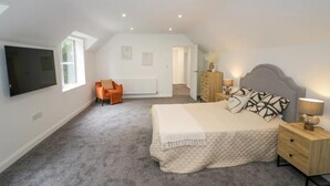 Un dormitorio con cama, televisor, silla, cómoda y radiador.