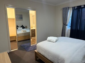 Un dormitorio con cama, armario, baño y ventana con cortinas.
