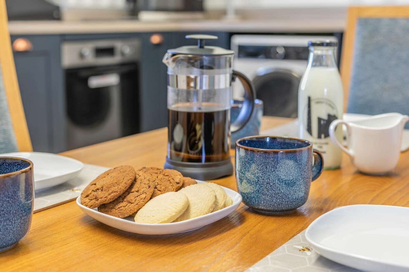 A breakfast setup with cookies, a coffee pot, and a milk jug on a wooden table.