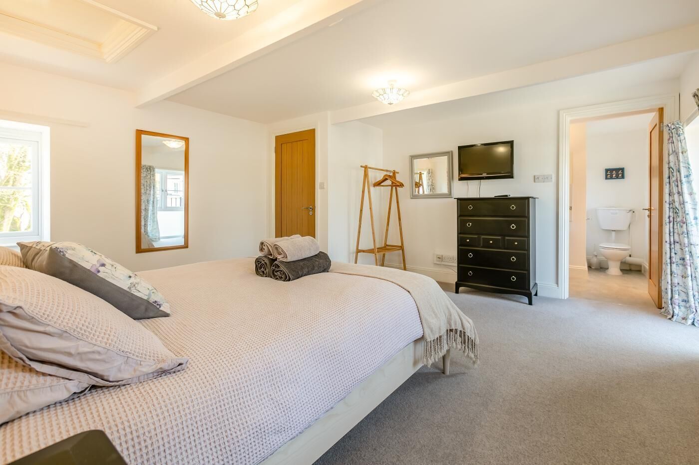 A bedroom with a large bed, a dresser, a television, and a bathroom visible through an open door.