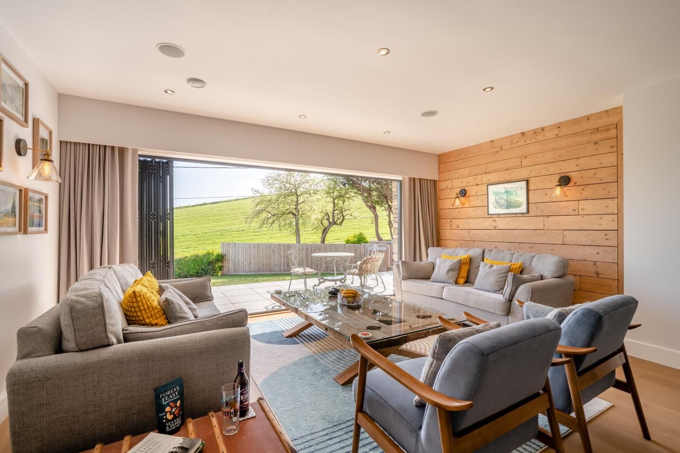 A modern living room with a glass coffee table, grey sofas, and a wooden wall.