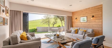 A modern living room with a glass coffee table, grey sofas, and a wooden wall.