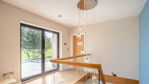 Un interior moderno con un vidrio corredizo que da a un balcón, una escalera de madera e iluminación colgante.
