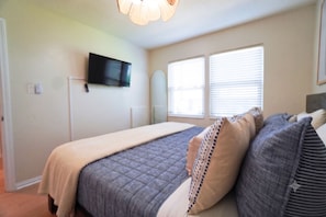 Een slaapkamer met een bed, een wandgemonteerde flatscreen televisie en een raam met zonwering.