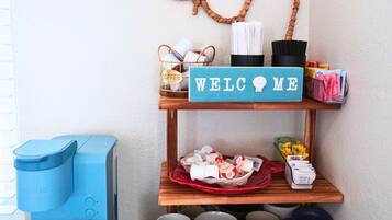 Ein Zimmer mit Wanddeko mit dem Schriftzug 'Beach', einem 'Welcome Me'-Schild, einer Kaffeemaschine, Tassen und einem Schild mit der Aufschrift 'Der Strand ist mein glücklicher Ort'.