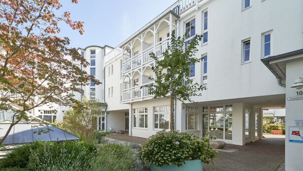 A white building with balconies, a garden area with plants, and a clear sky. - Moderne Ferienwohnung mit Zwei Schlafzimmern (Sellin)