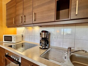 A kitchen with wooden cabinets, a microwave, a coffee maker, and a stainless steel sink. - Moderne Ferienwohnung mit Zwei Schlafzimmern (Sellin)