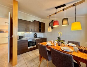 A modern kitchen with dark wooden cabinets, a built-in oven, and a dining area with a wooden table and chairs. - Moderne Ferienwohnung mit Zwei Schlafzimmern (Sellin)