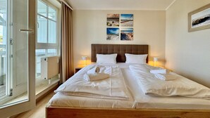 A double bed with white linens, a wooden headboard, and two bedside lamps. - Moderne Ferienwohnung mit Zwei Schlafzimmern (Sellin)