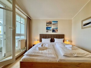 A double bed with white linens, a wooden headboard, and two bedside lamps. - Moderne Ferienwohnung mit Zwei Schlafzimmern (Sellin)