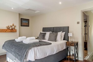 Cama bem arrumada com travesseiros e toalhas dobradas, mesa de cabeceira com abajur, e quadro na parede.