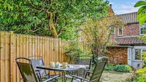 Eine Terrasse mit Tisch und Stühlen, ein Holzzaun und im Hintergrund ein Backsteinhaus.