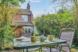 A glass table with a teapot, a cup, and a book in a garden setting with a brick house in the background. - 2 Bed in Cherry Burton (oc-c37535) (Cherry Burton)