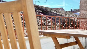 A balcony with a metal railing, a wooden chair, and a view of a stone building with multiple antennas.