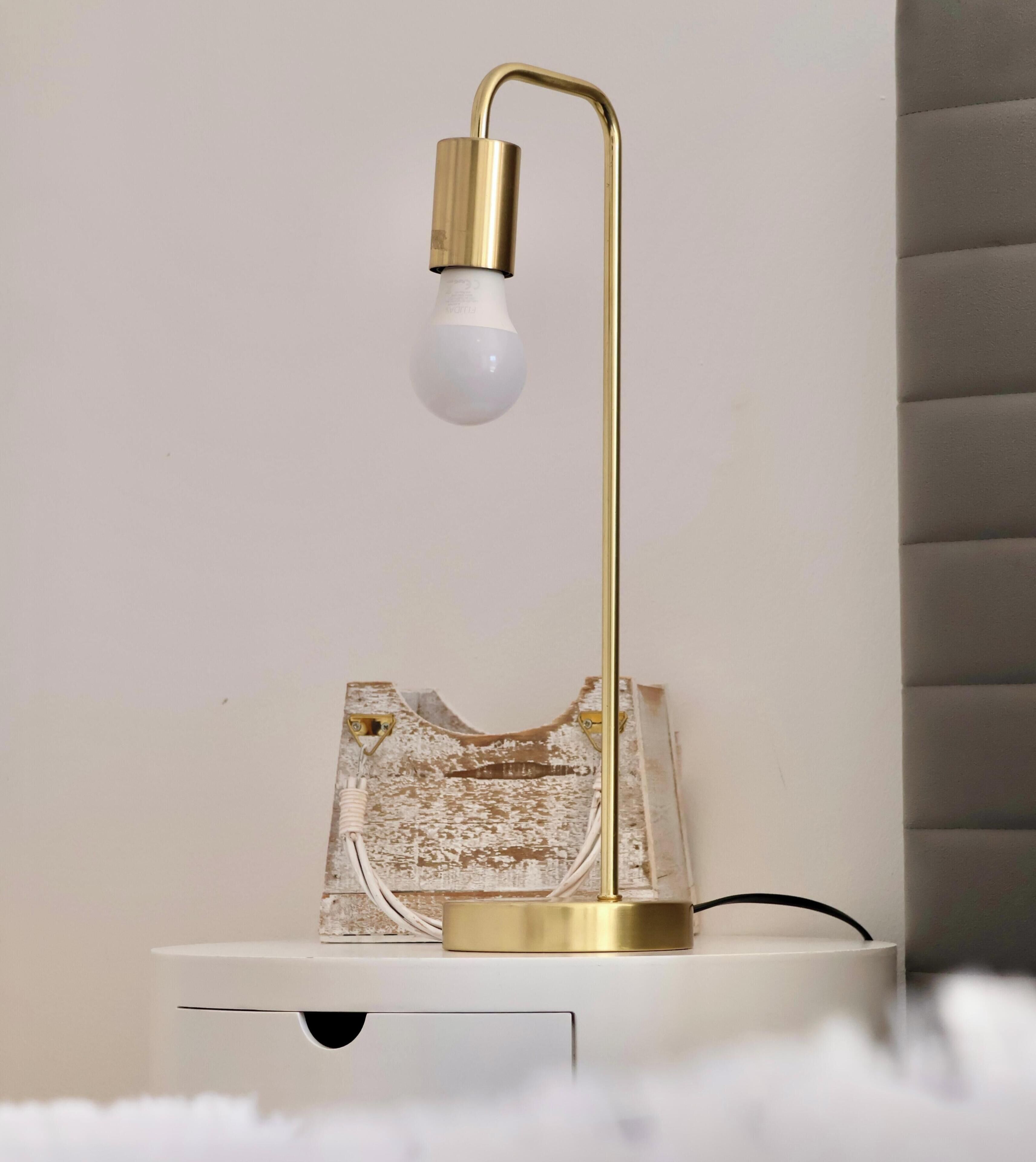 A white bedside table with a gold lamp featuring a white bulb.
