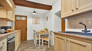 A kitchen with wooden cabinets, a dining table with chairs, a clock on the wall, and a hanging pendant light. - 2 Bed in Gunnerside (oc-g37866) (Gunnerside)