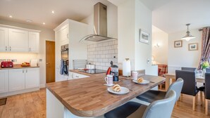 Una cucina moderna con mobili bianchi, un piano di lavoro in legno e una zona pranzo con tavolo e sedie.