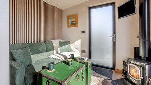 A modern living room with a sofa, a green chest of drawers, a fireplace, a television, and a sliding glass door. - 1 Bed in Austwick (oc-b37509) (Austwick)