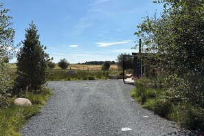 A gravel path leading to a metal gate, surrounded by greenery and a clear sky.