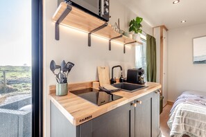 A compact kitchen with a built-in stove, a sink, and a window overlooking a grassy area. - 1 Bed in Austwick (oc-b37509) (Austwick)