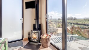 A modern room with a wood-burning stove, a television mounted on the wall, and a large glass door leading to an outdoor area. - 1 Bed in Austwick (oc-b37509) (Austwick)