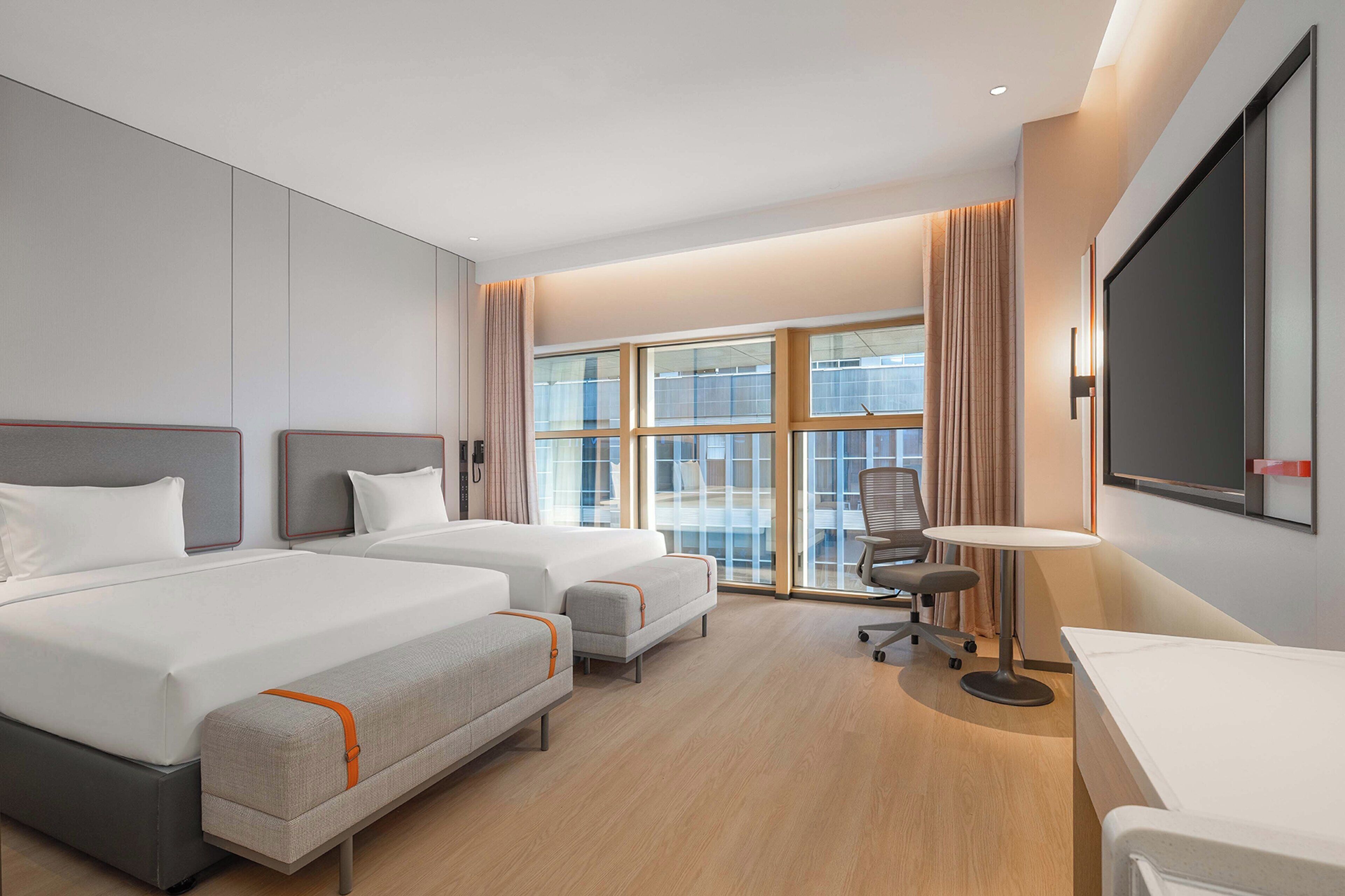 Ein Hotelzimmer mit zwei Betten, einem Schreibtisch, einem Stuhl und einem großen Fenster.
