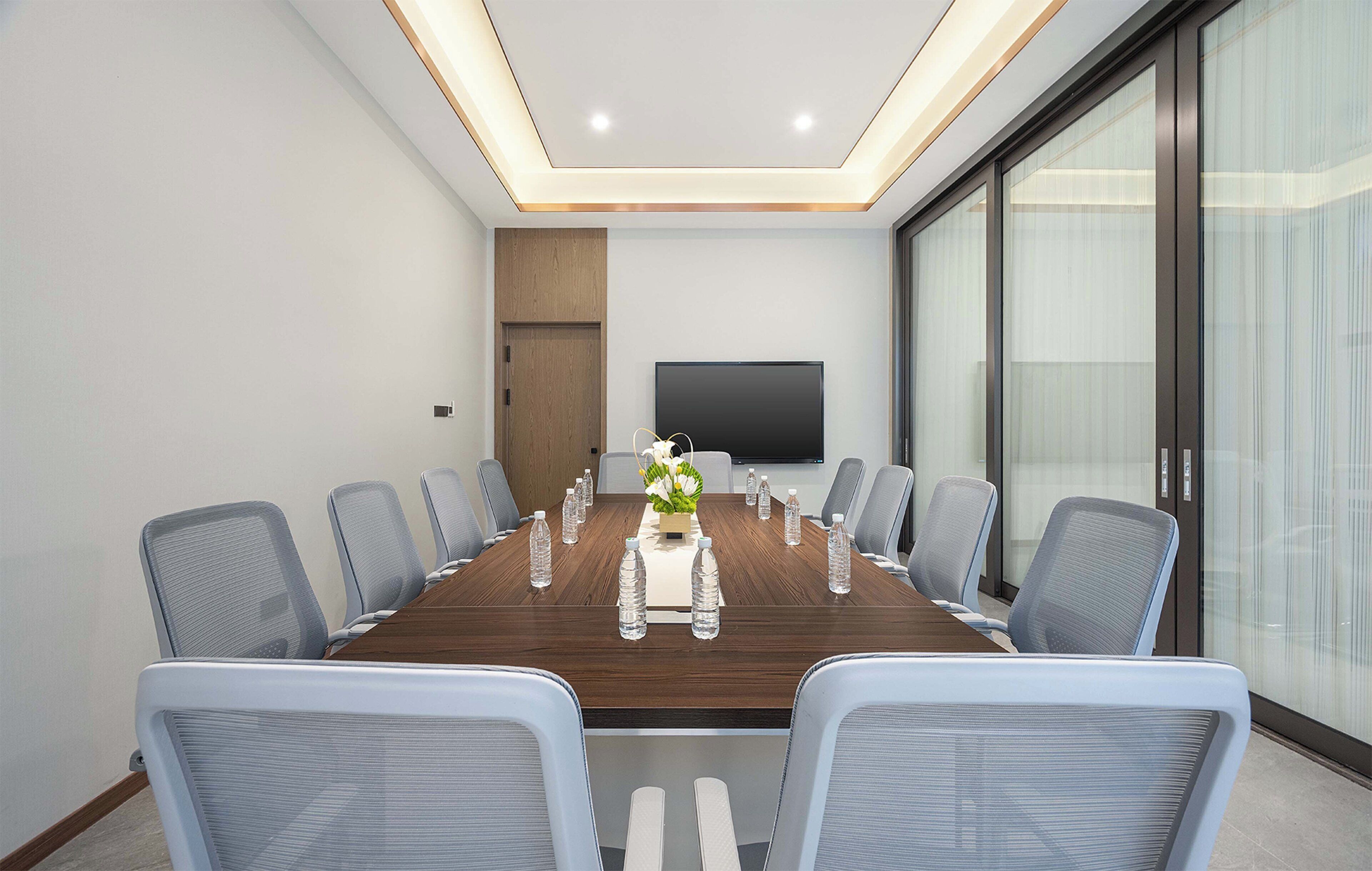 Un salón de conferencias con una larga mesa, sillas, una pantalla de televisión y un muro de vidrio.