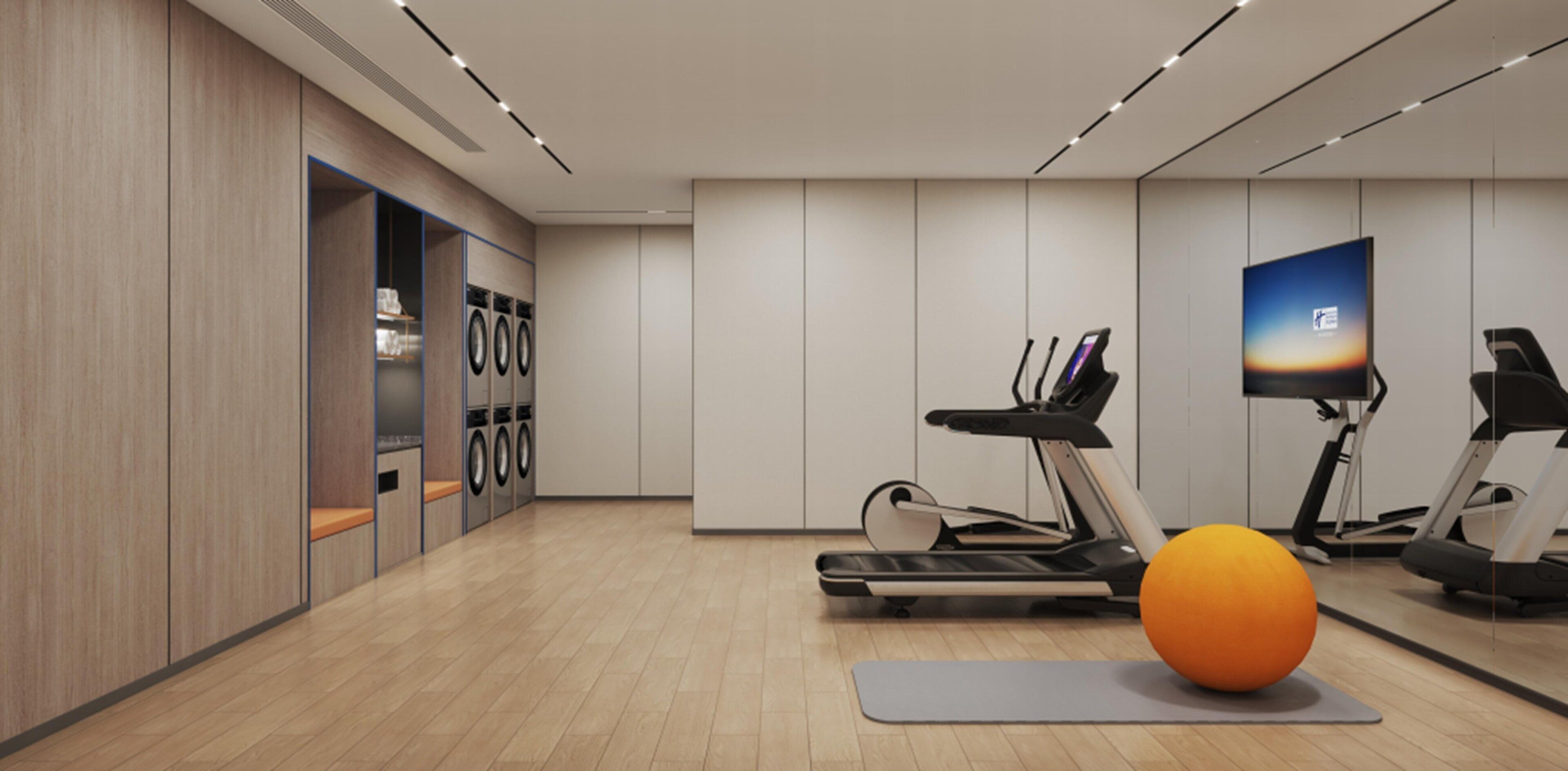 A modern gym with a treadmill, elliptical, stationary bike, and a large orange exercise ball.