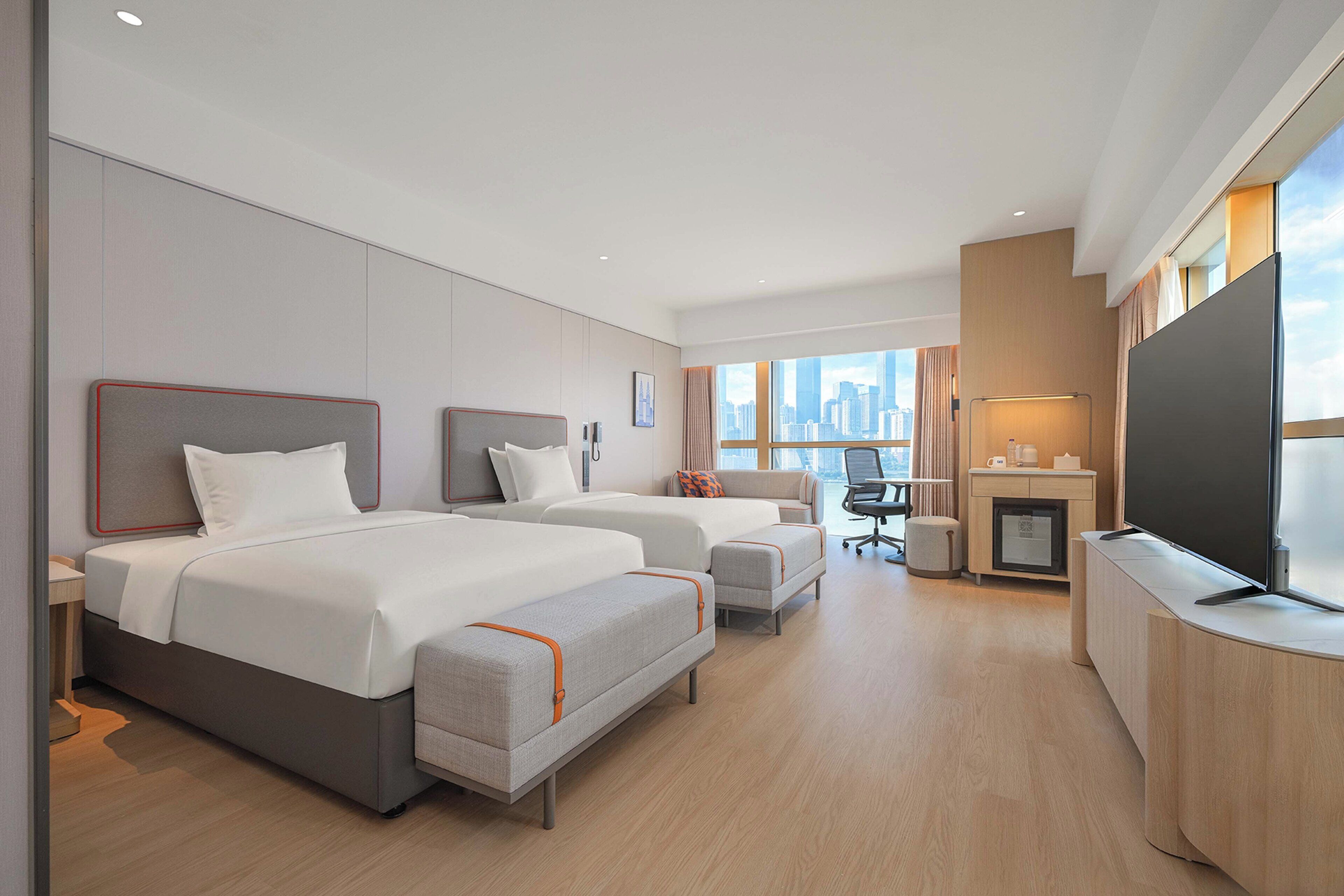 A hotel room with two beds, a desk, a TV, and a city view.