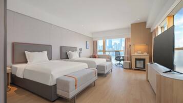 A hotel room with two beds, a desk, a TV, and a city view.