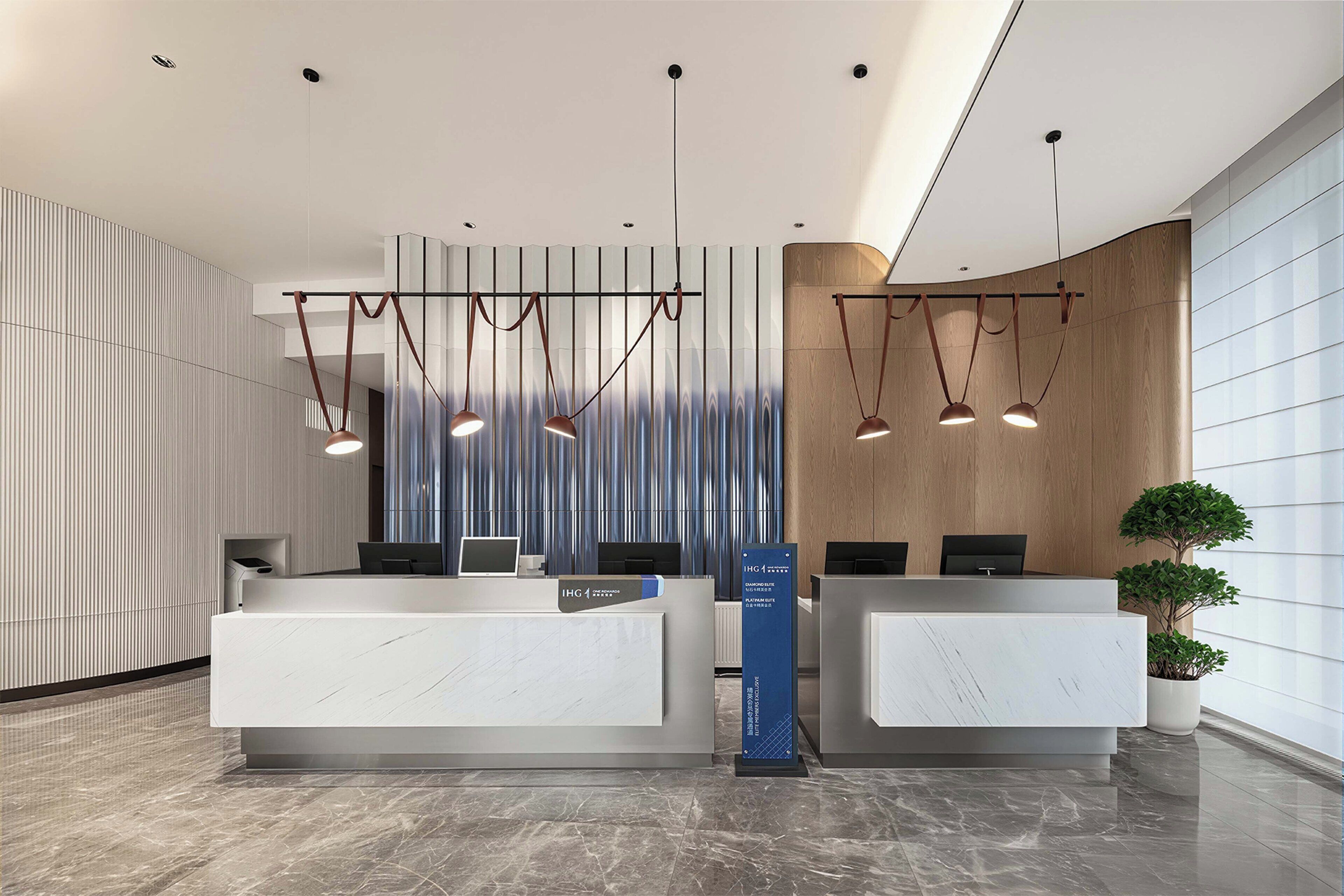 A reception desk with two computer stations, a vertical light fixture, and a potted plant.