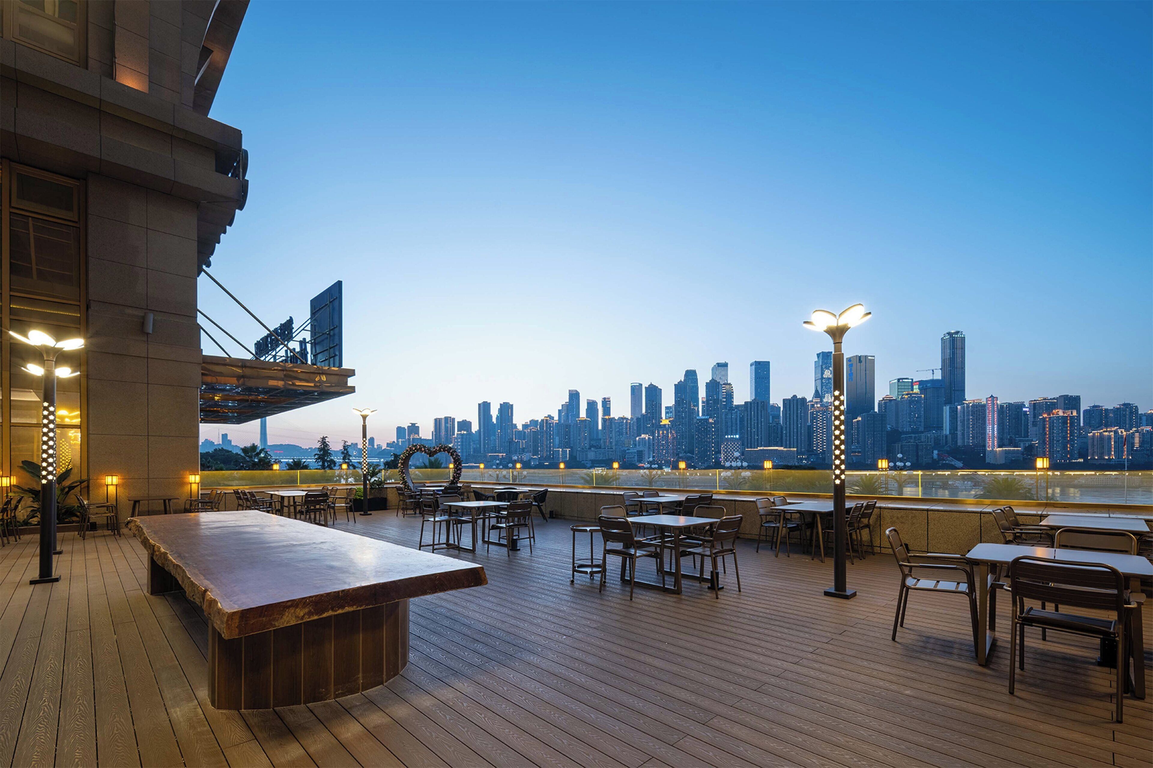 An outdoor dining area with tables and chairs, overlooking a city skyline at dusk.