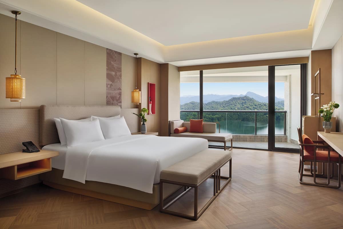 A modern hotel room with a large bed, a desk, and a balcony with a mountain view.