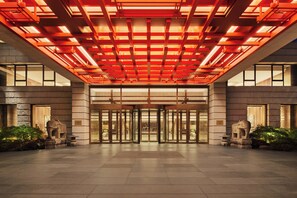En hotellentrén med modern design, med en stor glasdörr, ett rött upplyst tak och statyer av elefanter i sten.