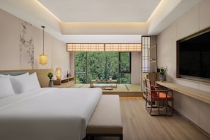 A modern hotel room with a large bed, a desk, a TV, and a view of the outdoors.