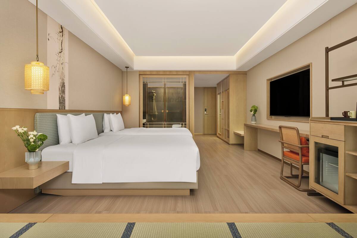 A modern hotel room with a large bed, a TV, a desk, and a seating area.