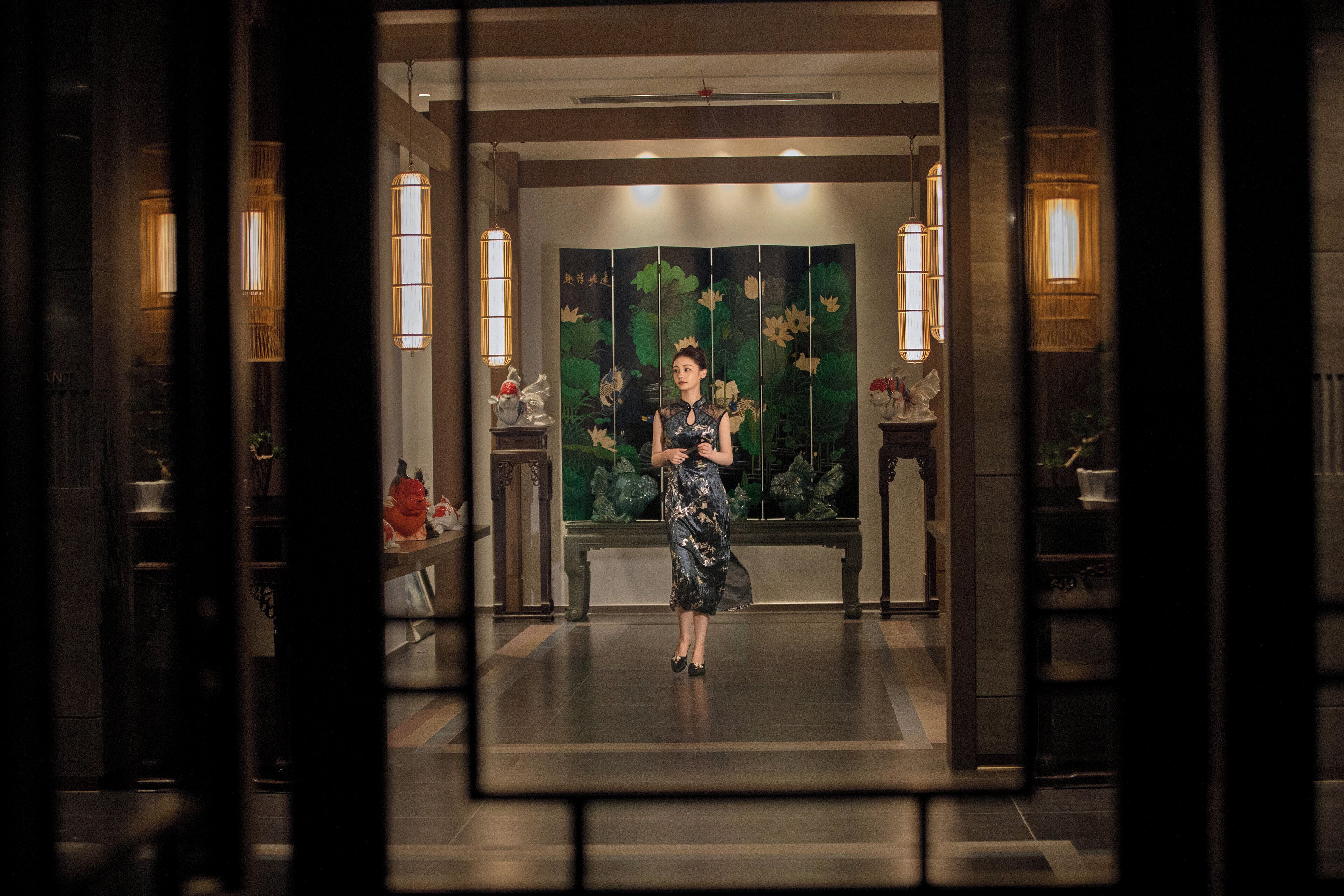 A woman standing in a lobby with a traditional backdrop, a bench, and decorative lighting.